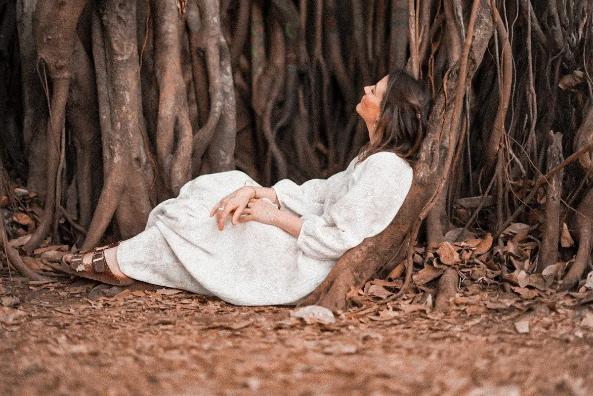Femme apaisée adossée à un arbre, visage levé vers la lumière